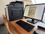 Arbeitsplatz in der Steiermärkischen Landesbibliothek mit Computer, Tastatur, Maus und Drucker. Auf dem Bildschirm ist ein historisches Dokument sichtbar.